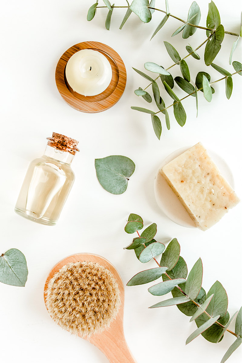 An image of various items like sented oil, a candle, multiple stems with leaves, a brush, and soap.